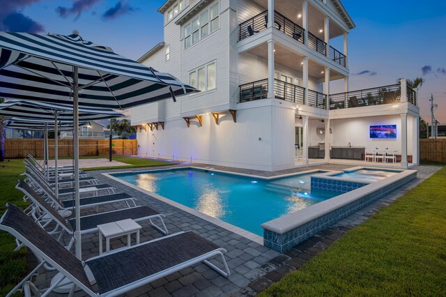 pool at dusk with an in ground hot tub and a patio