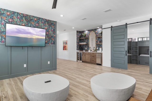 living room with sink, light hardwood / wood-style flooring, a barn door, and beverage cooler