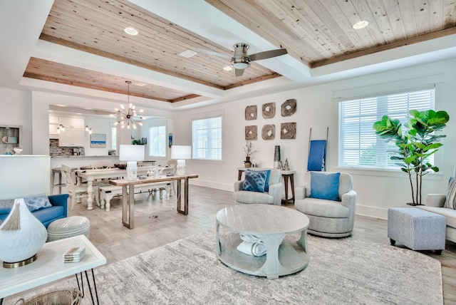 living room with a tray ceiling, ceiling fan with notable chandelier, and light wood-type flooring