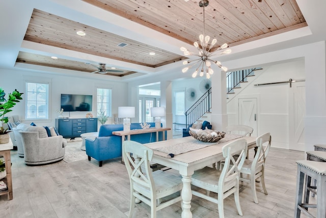 dining room featuring ceiling fan with notable chandelier, a barn door, light hardwood / wood-style floors, and a raised ceiling