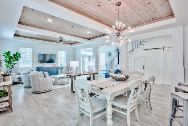 dining space featuring wood ceiling, ceiling fan with notable chandelier, a raised ceiling, a barn door, and light hardwood / wood-style flooring