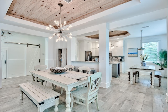 dining area featuring a tray ceiling, a barn door, light hardwood / wood-style floors, and a notable chandelier