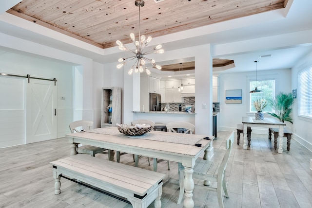 dining room featuring light wood-type flooring, a barn door, an inviting chandelier, and a raised ceiling