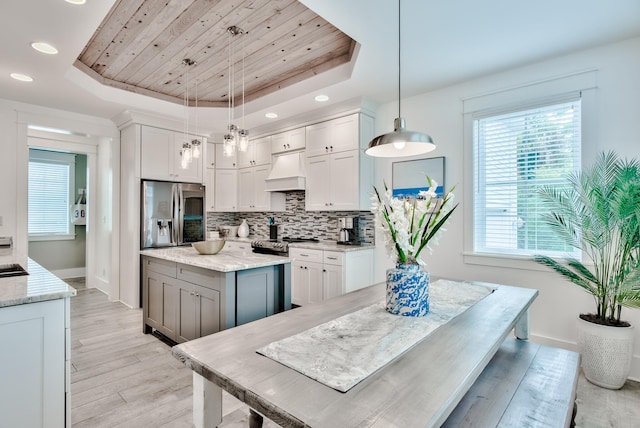 kitchen featuring white cabinets, decorative light fixtures, stainless steel fridge, and a tray ceiling