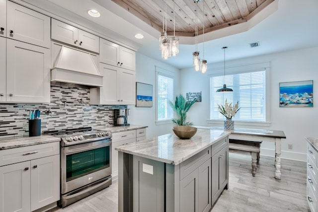 kitchen featuring light stone countertops, custom range hood, a raised ceiling, hanging light fixtures, and stainless steel electric range