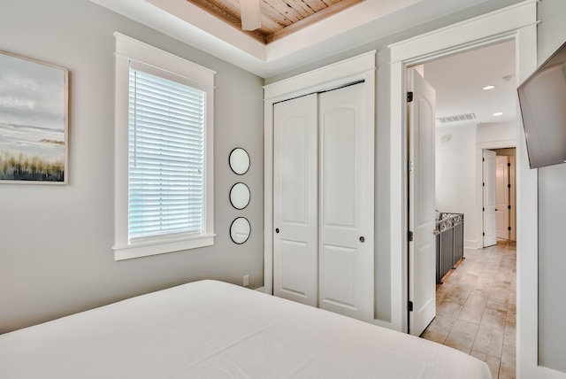 bedroom featuring wood ceiling, a raised ceiling, ceiling fan, light hardwood / wood-style flooring, and a closet