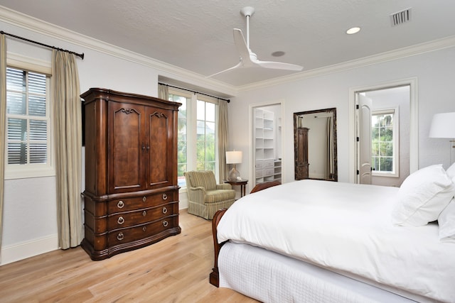 bedroom featuring a walk in closet, ceiling fan, light hardwood / wood-style flooring, and crown molding