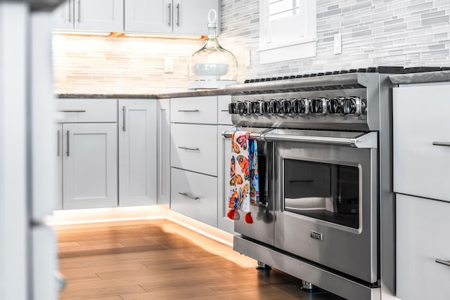 kitchen with white cabinetry, double oven range, light stone counters, and decorative backsplash