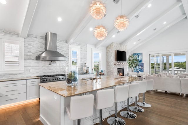 kitchen with sink, wall chimney range hood, white cabinets, and beam ceiling