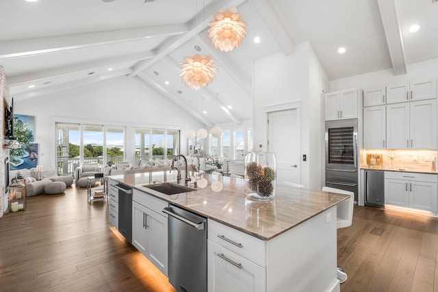 kitchen featuring sink, light stone counters, tasteful backsplash, high vaulted ceiling, and a kitchen island with sink