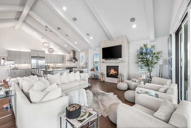 living room featuring dark hardwood / wood-style floors, high vaulted ceiling, sink, a large fireplace, and beam ceiling