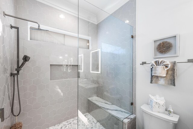 bathroom with ornamental molding, a tile shower, and toilet