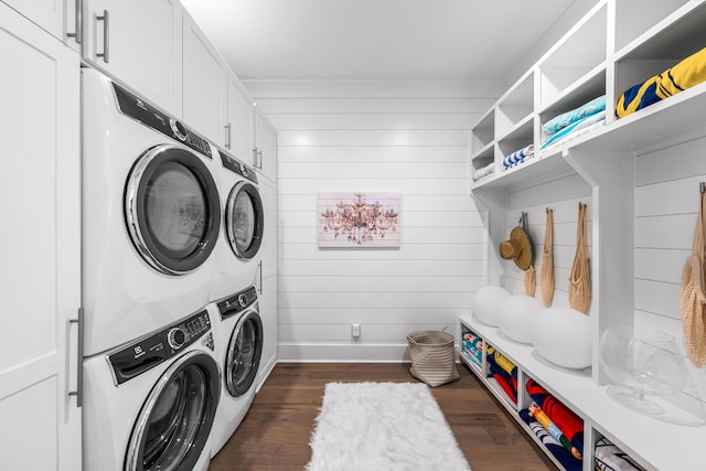 laundry room featuring cabinets, stacked washer and clothes dryer, dark hardwood / wood-style flooring, and wood walls