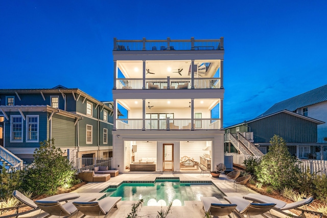 back house at night with ceiling fan, a balcony, an outdoor hangout area, and a patio