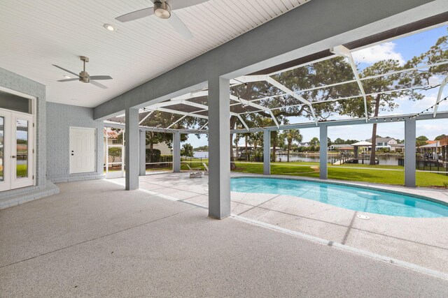 view of swimming pool with a lanai, ceiling fan, a water view, a patio, and a lawn