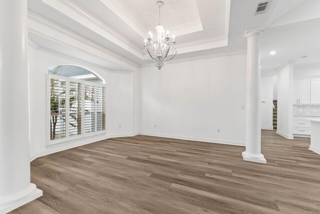 empty room featuring an inviting chandelier, a raised ceiling, decorative columns, crown molding, and hardwood / wood-style floors