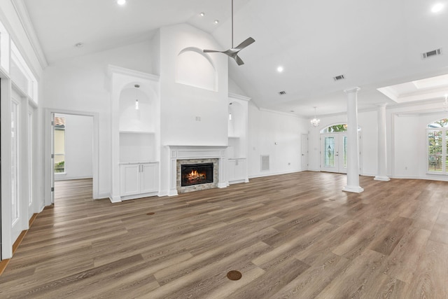 unfurnished living room featuring ceiling fan with notable chandelier, a stone fireplace, dark hardwood / wood-style floors, a towering ceiling, and decorative columns