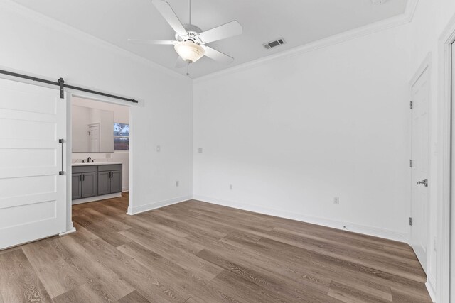 interior space featuring ceiling fan, a barn door, crown molding, ensuite bathroom, and light hardwood / wood-style floors