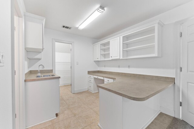 kitchen featuring kitchen peninsula, sink, white cabinetry, a breakfast bar area, and light tile patterned flooring