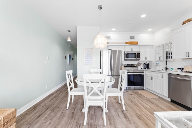 kitchen with appliances with stainless steel finishes, light hardwood / wood-style flooring, white cabinets, and pendant lighting