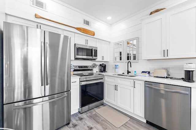 kitchen with white cabinets, light wood-type flooring, ornamental molding, sink, and appliances with stainless steel finishes