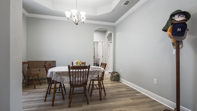 dining room featuring crown molding, a raised ceiling, an inviting chandelier, and hardwood / wood-style flooring