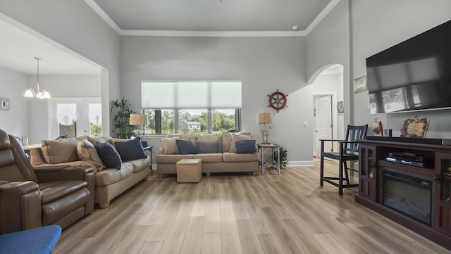 living room featuring a high ceiling, crown molding, an inviting chandelier, and light hardwood / wood-style flooring