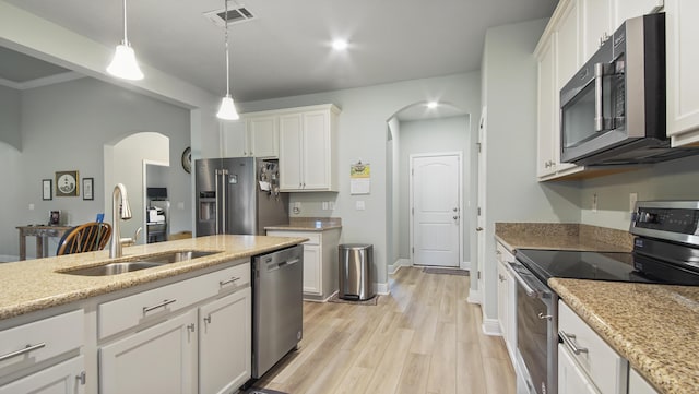 kitchen with appliances with stainless steel finishes, decorative light fixtures, white cabinetry, sink, and light wood-type flooring