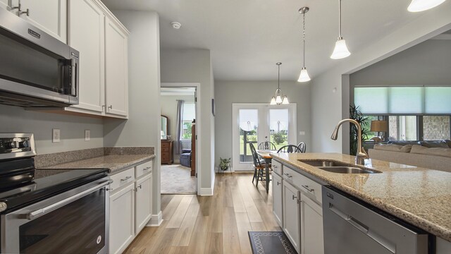 kitchen featuring stainless steel appliances, sink, white cabinets, and decorative light fixtures