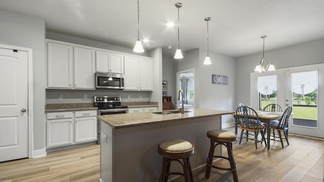 kitchen with appliances with stainless steel finishes, decorative light fixtures, sink, white cabinets, and a kitchen island with sink