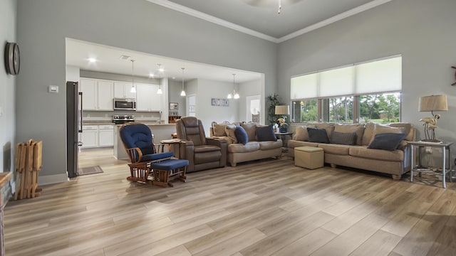 living room with a high ceiling, crown molding, ceiling fan with notable chandelier, and light wood-type flooring