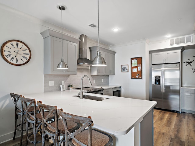 kitchen featuring appliances with stainless steel finishes, gray cabinetry, wall chimney range hood, hanging light fixtures, and dark wood-type flooring