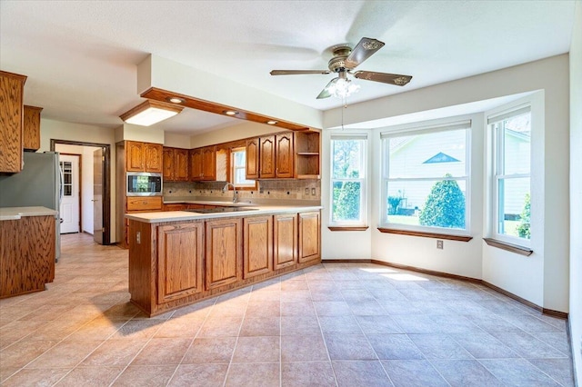 kitchen with ceiling fan, backsplash, kitchen peninsula, light tile patterned flooring, and appliances with stainless steel finishes