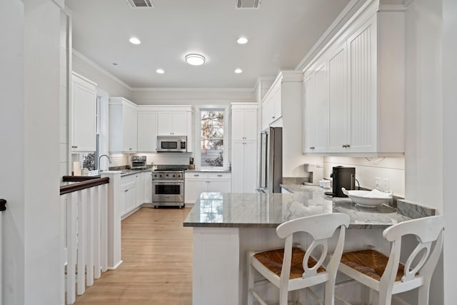 kitchen featuring a breakfast bar area, white cabinetry, kitchen peninsula, stainless steel appliances, and light stone countertops