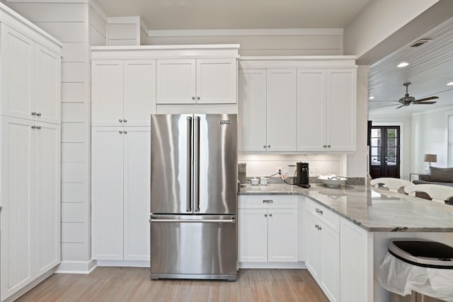 kitchen featuring white cabinets, ceiling fan, light stone counters, high end fridge, and light hardwood / wood-style flooring