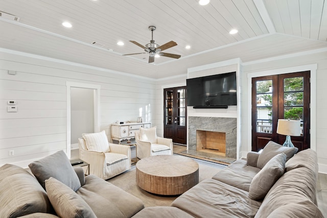 living room featuring french doors, wood walls, wood ceiling, crown molding, and a premium fireplace