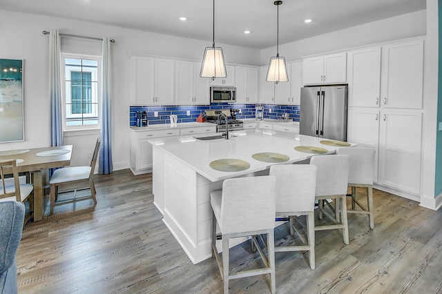 kitchen featuring white cabinetry, light wood-type flooring, appliances with stainless steel finishes, and a center island with sink