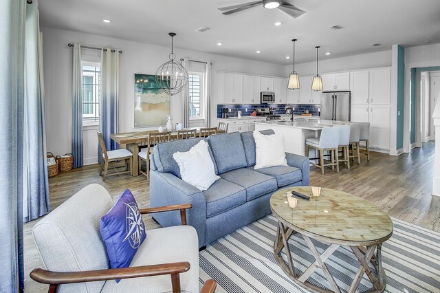 living room featuring light hardwood / wood-style floors, a wealth of natural light, and ceiling fan with notable chandelier