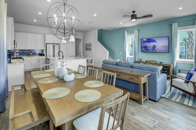 dining space featuring sink, ceiling fan with notable chandelier, light hardwood / wood-style flooring, and a wealth of natural light