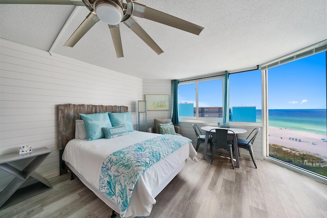 bedroom with a textured ceiling, a view of the beach, a water view, wood finished floors, and a wall of windows