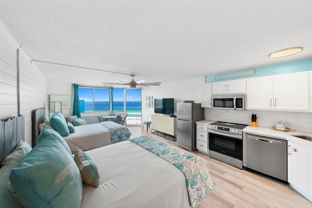 kitchen featuring light countertops, light wood-style flooring, appliances with stainless steel finishes, open floor plan, and white cabinetry