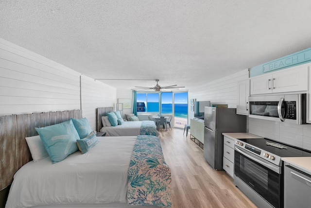 bedroom with light wood finished floors, a ceiling fan, freestanding refrigerator, access to outside, and expansive windows