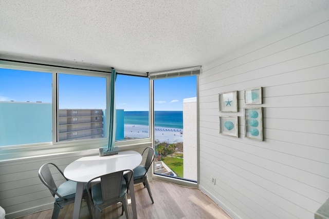 dining room with a textured ceiling, a water view, wood finished floors, and a view of the beach