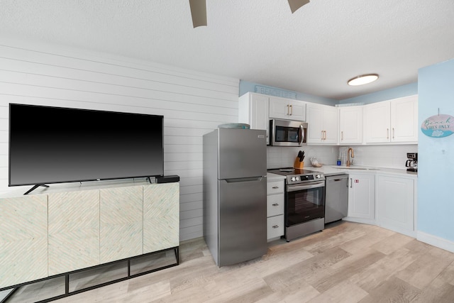 kitchen featuring white cabinets, appliances with stainless steel finishes, light countertops, light wood-style floors, and a sink