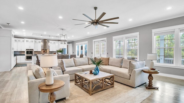 living room with light wood-type flooring, crown molding, and ceiling fan with notable chandelier