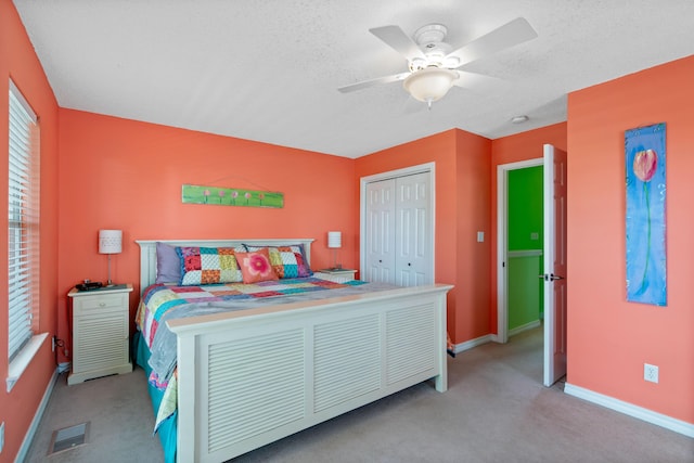 bedroom featuring ceiling fan, light colored carpet, a closet, and a textured ceiling