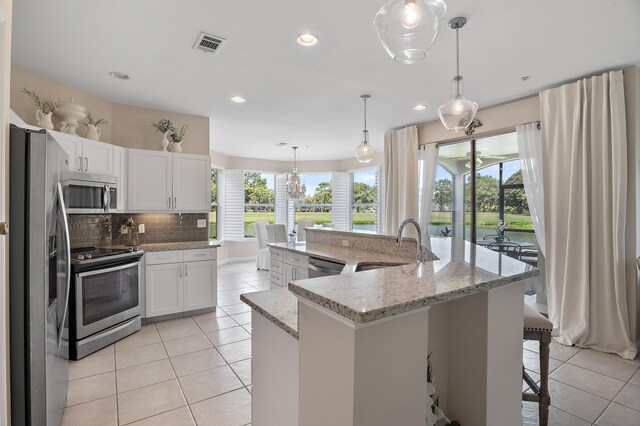 kitchen featuring appliances with stainless steel finishes, an island with sink, light tile patterned floors, and backsplash