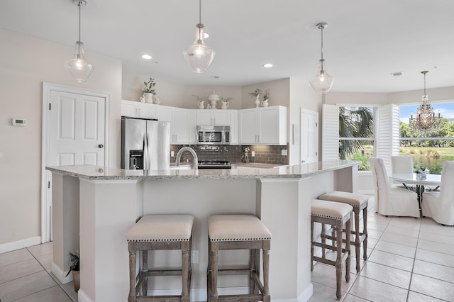 kitchen featuring white cabinetry, a kitchen bar, appliances with stainless steel finishes, light tile patterned floors, and backsplash