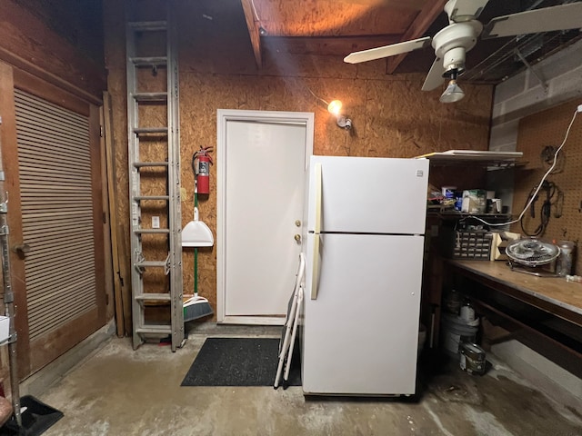 kitchen featuring concrete flooring, wood walls, ceiling fan, and white fridge