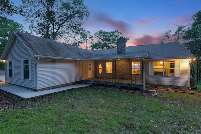 back house at dusk featuring a yard and central AC